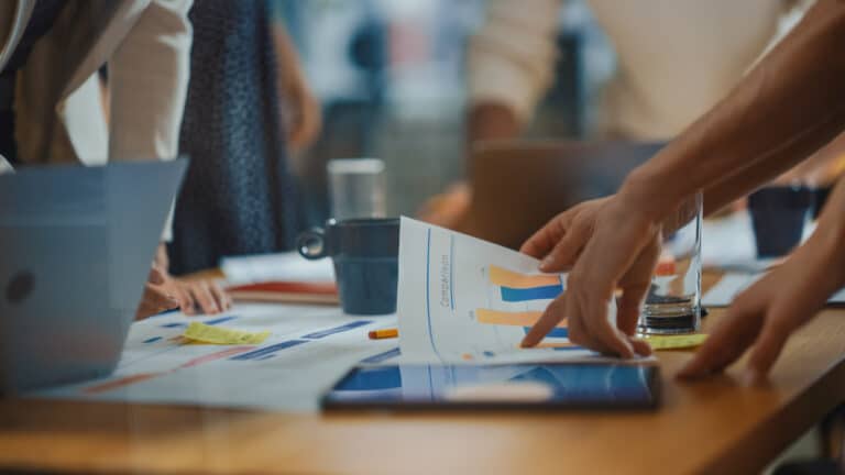 Group of people around table pointing at pages of data